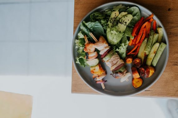 Top view of a vibrant platter with grilled skewers and fresh vegetables on a wooden table.